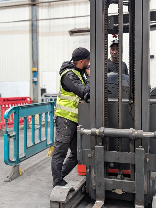 PPE-clad construction worker in durable safety gloves inspecting materials near a forklift.