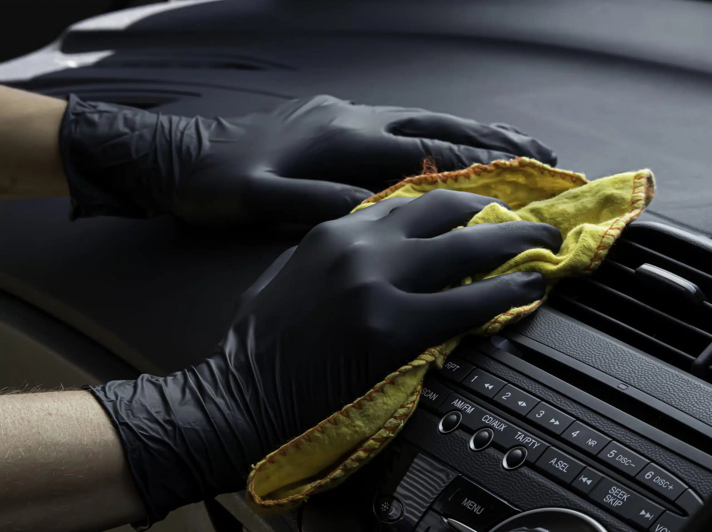 Person cleaning car interior with a yellow cloth and black nitrile gloves