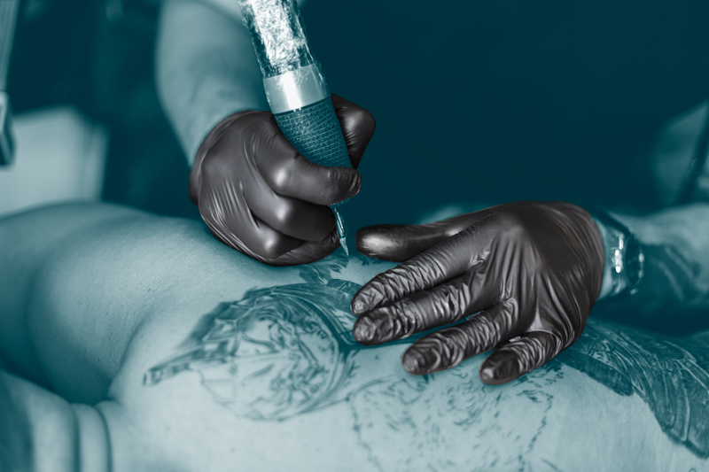 Person getting a tattoo with a tattoo artist's gloved hands and a tattoo machine.
